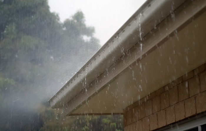 It is raining and the water is overflowing from the roof gutter