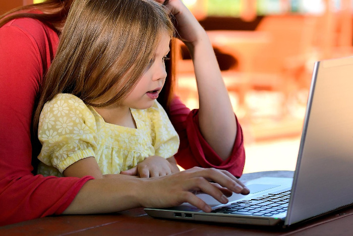 Young girl sitting on a woman's lap, both looking at a laptop screen