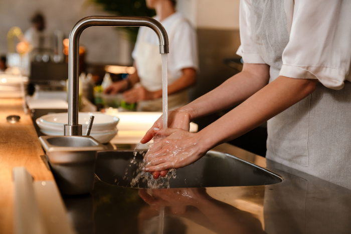 Young white chef woman wearing apron washing hands while working in restaurant kitchen